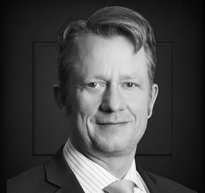 Man wearing a suit jacket, white shirt, and tie, with neatly styled hair.